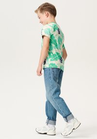 Groene kortmatige t-shirt metbladmotieven, gecombineerd met lichtblauwe opgerolde spijkerbroek en witte sneakers met mintaccenten.