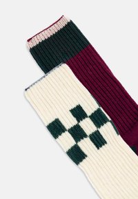 Calze a maglia con motivi a costine in verde scuro e bordeaux, con una sezione crema che presenta dettagli a quadretti verdi.