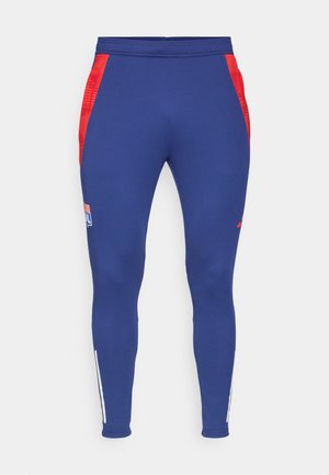 Pantaloni sportivi blu navy con pannelli laterali rossi, un logo sulla coscia e strisce bianche alla caviglia. Realizzati in un tessuto elastico e liscio.