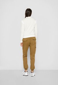 Lys grå hettegenser med hvite skulderdetaljer, kombinert med brune cargo-bukser med sidelommer, båret med hvite joggesko.