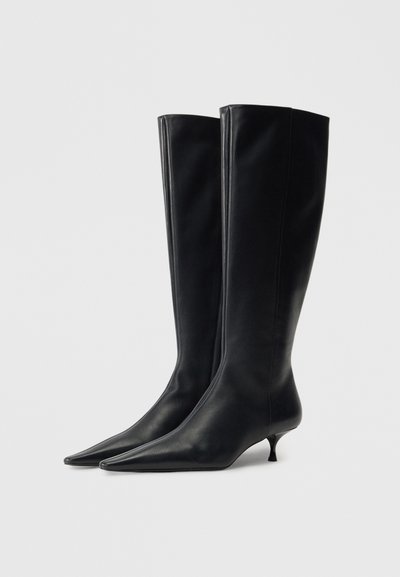 Juoda odinė iki kelių aukšta avalynė su smailiu pirštu ir plonu kitten kulniuku, pasižyminti lygiu paviršiumi ir elegantišku, prigludusiu dizainu.