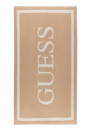 Beige rechthoekige handdoek met witte rand en de merknaam GUESS in grote witte letters verticaal gedrukt.