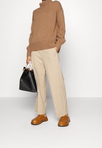 Brązowy gruby golfowy sweter z dzianiny, jasnobeżowe dopasowane spodnie, brązowe buty na platformie oraz czarna torebka z białymi akcentami.