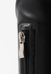 Sac noir texturé avec une fermeture éclair en métal sur le côté, une finition lisse et des détails de couture visibles.