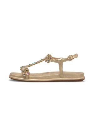 Sandalia plana dorada con tira en el tobillo, tira en T adornada con adornos de piedras preciosas multicolores y cierre de hebilla sobre fondo blanco.