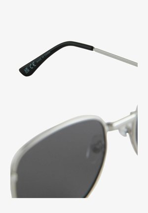 Lunettes de soleil argentées avec des verres sombres, dotées d'une branche noire élégante et d'accents en métal. La branche présente le texte "CE" et "FABRIQUÉ EN CHINE."