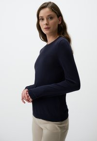 Maglione blu navy con maniche lunghe, scollo rotondo e polsini a coste, realizzato in un tessuto morbido, abbinato a pantaloni chiari.