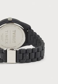 Black rubber watch with a silver stainless steel clasp, round face, and a textured band. Displays "Timex" and water-resistant details on back.