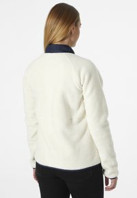 Chaqueta de forro polar en color blanco roto con un exterior texturizado, cuello azul marino y detalles negros en el dobladillo y los puños. Presenta mangas raglán y un ajuste relajado.