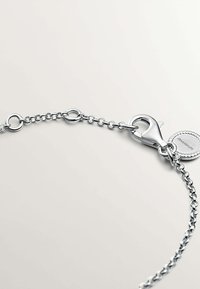Pulsera de cadena de plata con eslabones redondos, un cierre de langosta y un charm circular con detalles en relieve. Acabado metálico suave.