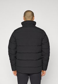 Giacca imbottita nera con colletto alto e design a cuciture orizzontali, con una texture liscia e un fitting leggermente rilassato.