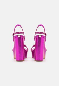 Tacones de plataforma metálicos fucsias con correas trenzadas y un tacón grueso, que presentan un acabado texturizado y un seguro hebilla en el tobillo.