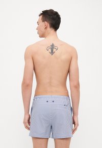 Shorts da nuoto a righe con un motivo blu e bianco, vita elastica e tasche laterali. Il tessuto sembra leggero e traspirante.