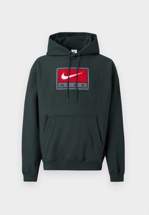 Sweat à capuche vert foncé en tissu doux, avec un grand logo Nike rouge et blanc sur un patch rectangulaire orné d'accents gris. Poche kangourou à l'avant.
