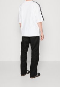 Bílý tričko s krátkým rukávem a černými bočními pruhy, v kombinaci s černými kalhotami a černými botami s bílými pruhy na straně.