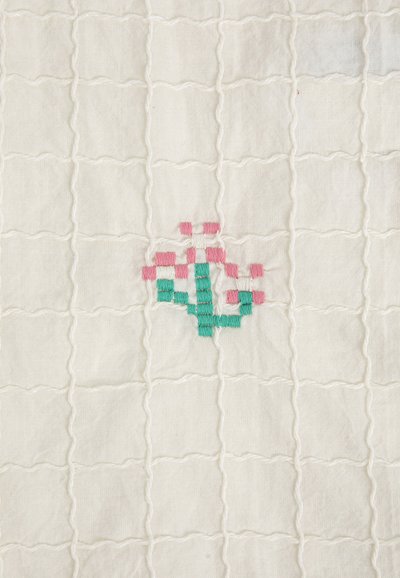 Tissu blanc matelassé avec un motif en quadrillage et une petite fleur brodée pixelisée rose et verte au centre.