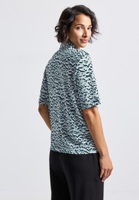 Top a maniche corte in un tessuto azzurro chiaro con un motivo astratto scuro. Vestibilità rilassata con scollo rotondo e texture morbida.
