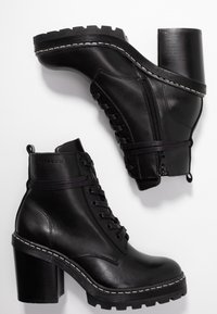 Svarta läderankelstövlar med en kraftig klack, snörning framtill, sidodragkedja, framträdande sömmar och en robust sula.