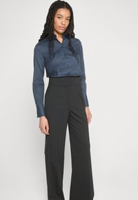 Camicia button-up in satin blu scuro con colletto, maniche lunghe e design cropped, abbinata a pantaloni neri a vita alta con gamba ampia.