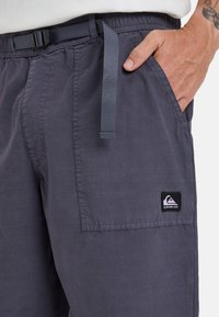 Grijze korte broek van lichtgewicht stof, met een elastische tailleband met riem, zijzakken en een zwarte logoplaat aan de zijkant.