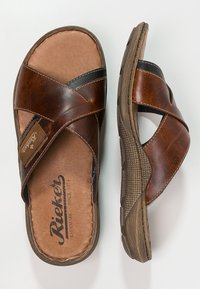 Sandales en cuir marron avec des brides croisées, une semelle texturée et une semelle intérieure rembourrée arborant le logo de la marque. Ajustement réglable pour plus de confort.