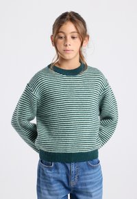 Maglione a righe con filato verde e bianco, caratterizzato da un collo rotondo, vestibilità ampia e bordi e orlo a costine. Abbinato a jeans in denim.