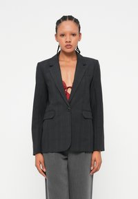 Blazer à carreaux noir avec une coupe ajustée, fermeture à un bouton et deux poches avant. Présente une texture lisse et des revers structurés.
