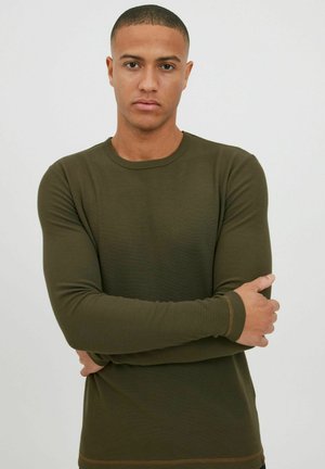 Camisa de manga larga verde oliva hecha de tejido acanalado. Presenta un escote redondo y un ribete en contraste en los puños y el dobladillo. Diseño ajustado.