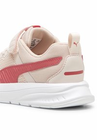Zapatilla deportiva de color rosa claro con parte superior de malla texturizada, acentos rojos contrastantes y suela de goma blanca. Incluye una lengüeta trasera.