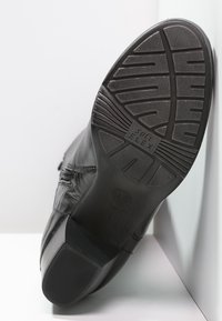 Zapato de cuero negro con una suela texturizada, que presenta surcos profundos y la etiqueta "SOFT FLEX." El zapato tiene un diseño elegante y un acabado suave.