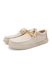 Baskets slip-on en toile beige avec un matériau texturé, lacets jaunes et un intérieur à motifs. Semelle en caoutchouc avec des bords striés.