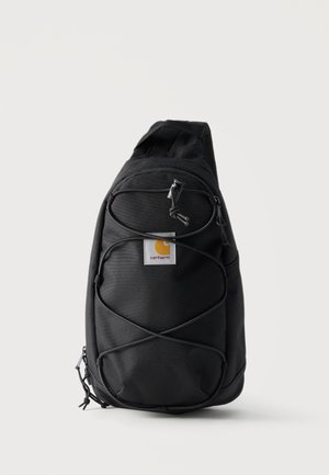Mochila tipo bandolera negra Carhartt con correa ajustable, bolsillo frontal con cremallera y cuerdas elásticas bungee sobre fondo blanco liso.