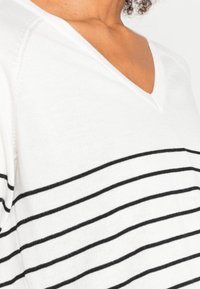 Biały top z dekoltem w serek z czarnymi poziomymi paskami, o miękkiej fakturze i lekkim materiale. Prosty i klasyczny design.