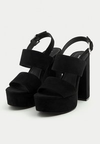 Black suede platform sandals with a chunky heel and open toe, featuring wide straps and an adjustable ankle buckle.