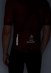 Rød cykeltrøje med korte ærmer, tekstureret stof og reflekterende lynlåslomme. Viser "TEAM BELGIUM" logoet på bagsiden.