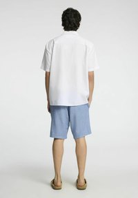 Bílá košile s krátkým rukávem, světle modré šortky a béžové sandály; jednoduchý design s volným střihem, texturou podobnou lnu a bez viditelných vzorů.