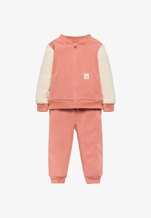 Chándal rosa que incluye una chaqueta con cremallera y mangas de forro polar crema, acompañada de pantalones rosa a juego con puños acanalados.