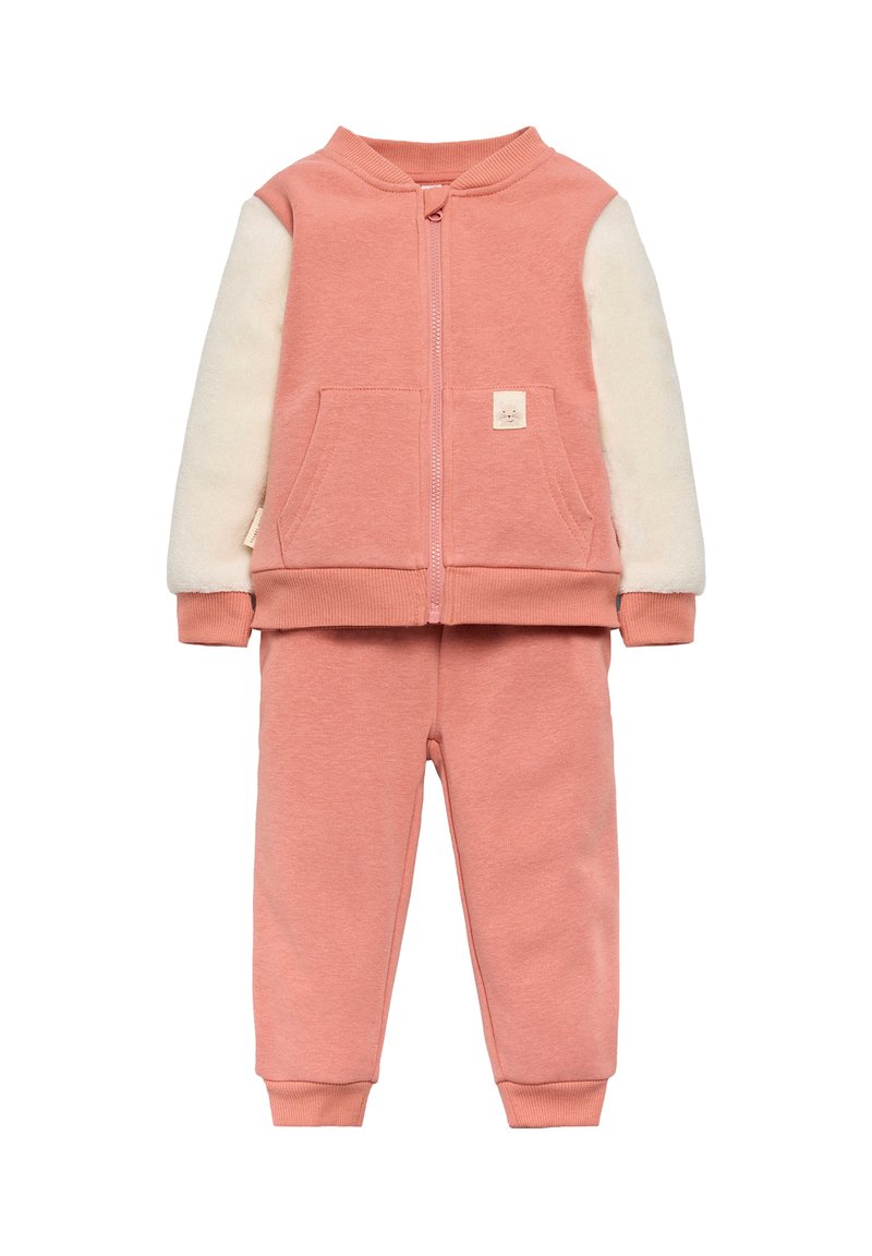 Chándal rosa que incluye una chaqueta con cremallera y mangas de forro polar crema, acompañada de pantalones rosa a juego con puños acanalados.