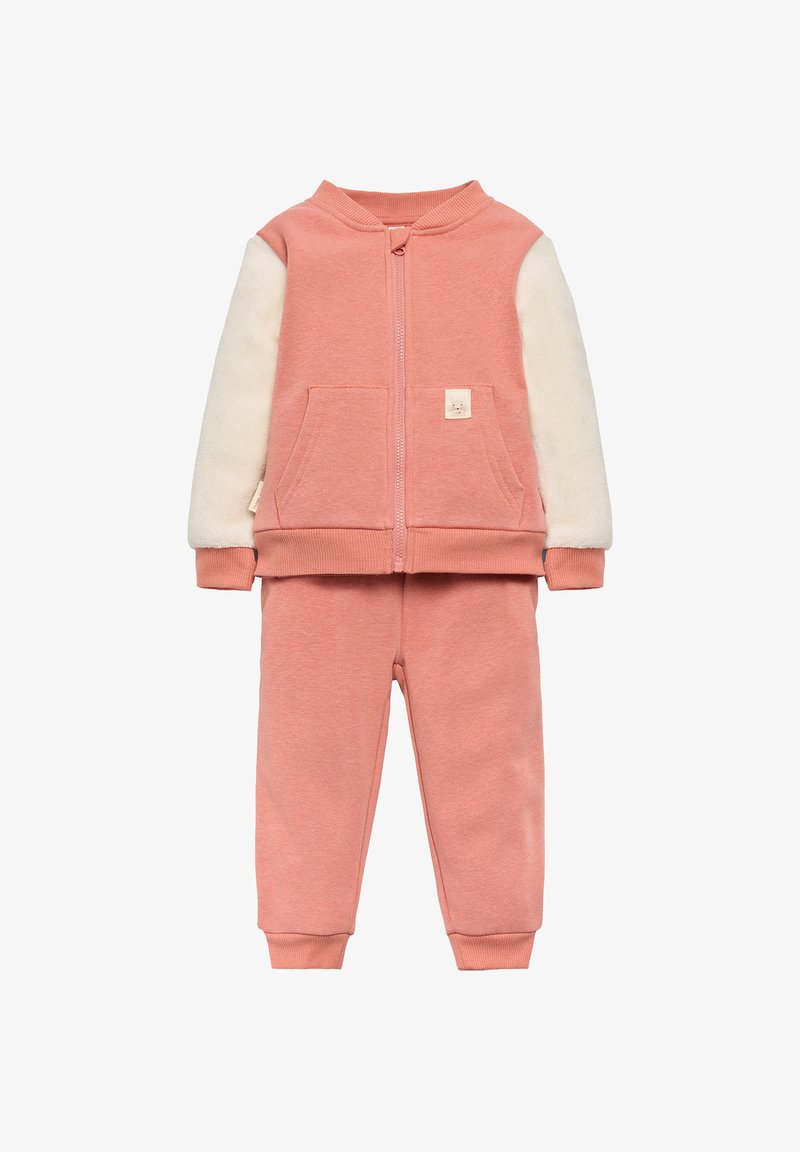 Chándal rosa que incluye una chaqueta con cremallera y mangas de forro polar crema, acompañada de pantalones rosa a juego con puños acanalados.