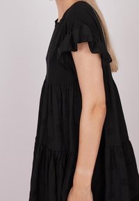 Robe noire à coupe décontractée, avec de courtes manches froncées et un design en étages. Fabriquée en tissu texturé avec des accents brodés subtils.