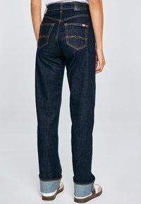 Jeans de mezclilla azul oscuro con costuras amarillas, que presentan dos bolsillos traseros y puños doblados hacia arriba para mostrar una tela de contraste.