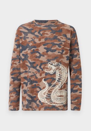 Μπλούζα παραλλαγής με μακριά μανίκια σε καφέ και σκούρο μπλε χρώμα με λεπτομερή γραφικό ενός λευκο-καφέ φιδιού που είναι τυλιγμένο στην κάτω δεξιά πλευρά μπροστά.