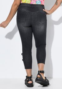 Pantalons capri en denim foncé à taille haute, avec des détails déchirés et des sangles à la cheville. Comprend deux poches arrière et une coupe slim, ajustée.