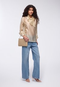Blusa di seta crema con un fiocco al colletto, abbinata a jeans a gamba ampia blu e una borsa a tracolla beige текстurizzata. Sandali con tacco trasparente.