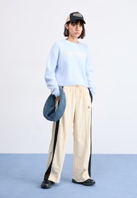 Lyseblå, fluffy, cropped genser med teksten "jordan", beige joggebukser med svarte striper, blå denimveske, svart caps og mørke sko.
