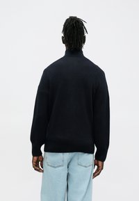 Camisola de malha de lã azul-marinho com gola alta falsa, ombros caídos e punhos canelados. Combinada com jeans oversized azul claro.