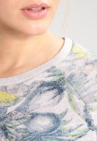 Pullover grigio chiaro con stampa floreale in tonalità di blu, verde e giallo. Presenta un collo a giro e un tessuto morbido e strutturato.