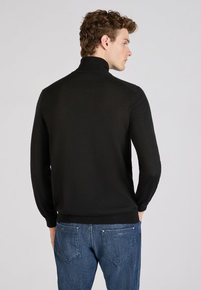 Zwarte pullovertrui met een hoge kraag en lange mouwen, voorzien van een gestructureerde stof. Gekenmerkt door blauwe jeans met achterzakken.