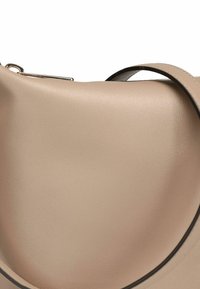 Sac à main en cuir beige avec une texture lisse, une forme incurvée et une sangle noire contrastante. Il est orné d'un détail en métal argenté.