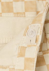 Beige and light brown plaid fabric with a button and visible stitching. Features a textured weave and clean edges, showcasing quality construction.